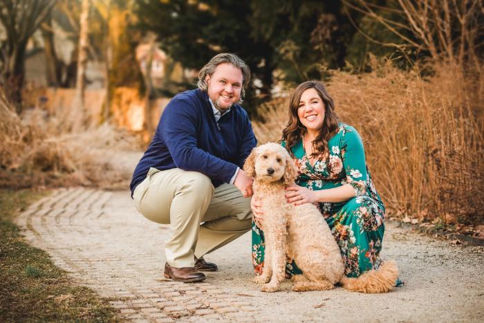 Man and woman kneeling on a path while holding a light-colored dog