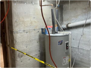 Water heater unit installed in a basement next to a concrete wall with caution tape