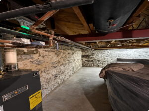 Basement interior featuring a black boiler, copper pipes, and a stone wall with a covered object.