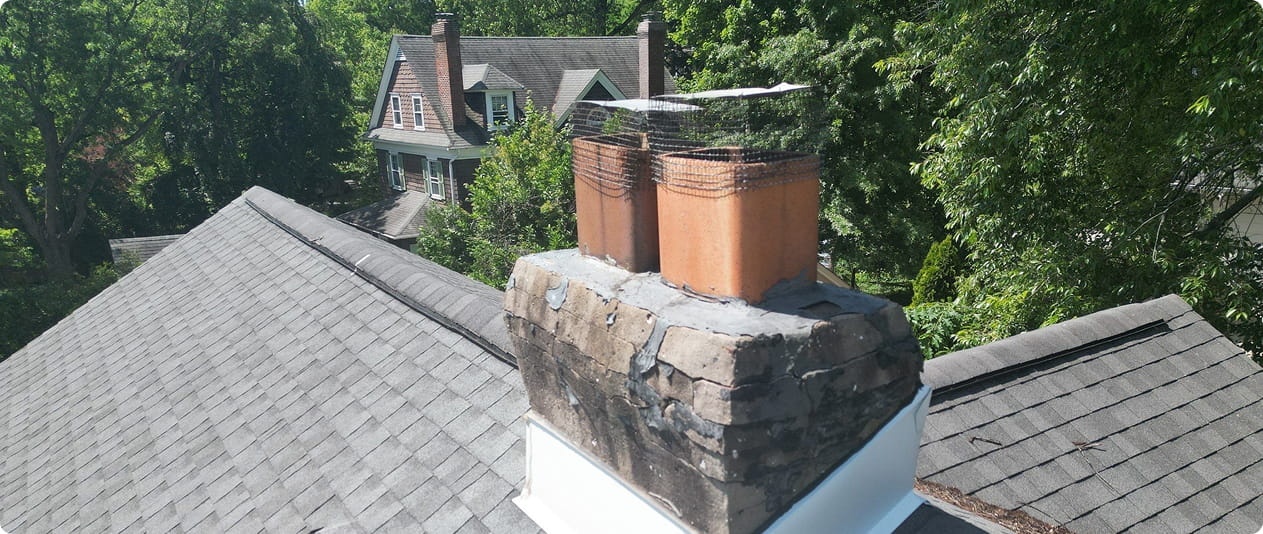 Stone chimney stack with two clay flue liners on a shingled roof