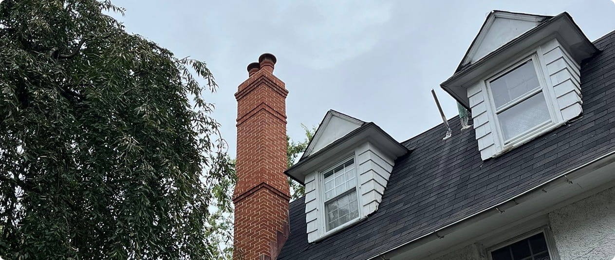 Tall red brick chimney rising above the roof of a house with white dormer windows.