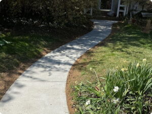 A curved concrete walkway leads through a grassy yard toward a house entrance.