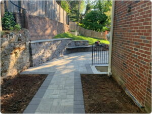 A paved patio area with a stone retaining wall and brick house exterior wall.