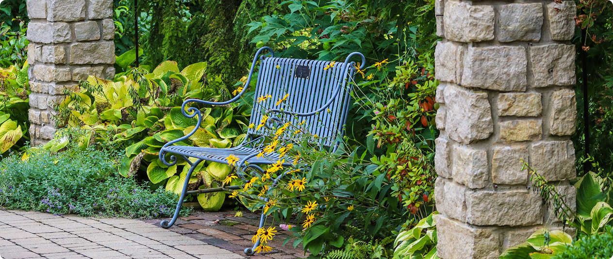 Blue metal bench positioned on a brick patio next to a stone pillar
